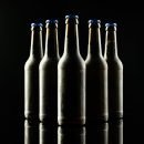 Horizontal image of five dark glass bottles of lager beer with blue crown caps on black background. Drinking alcohol, refreshment and lager day celebration concept.